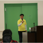 トレードマークの黄色いTシャツを着て講演する南雲代表